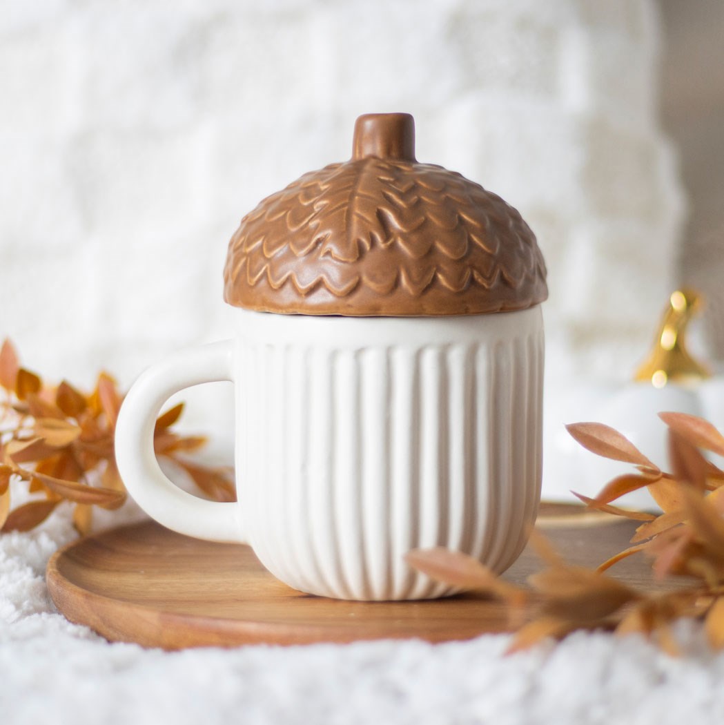 Autumn Acorn Ceramic Mug with Lid - White mug with a brown acorn-shaped lid on a wooden coaster with autumn leaves.
