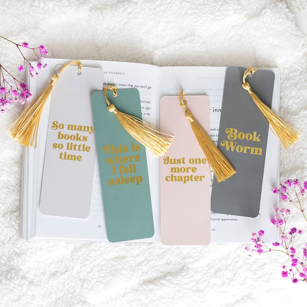 Four bookmarks with tassels on an open book, surrounded by pink flowers.