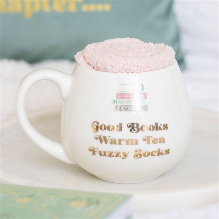 White mug with text 'Good Books Warm Tea Fuzzy Socks' and a pair of pink fluffy socks on top.