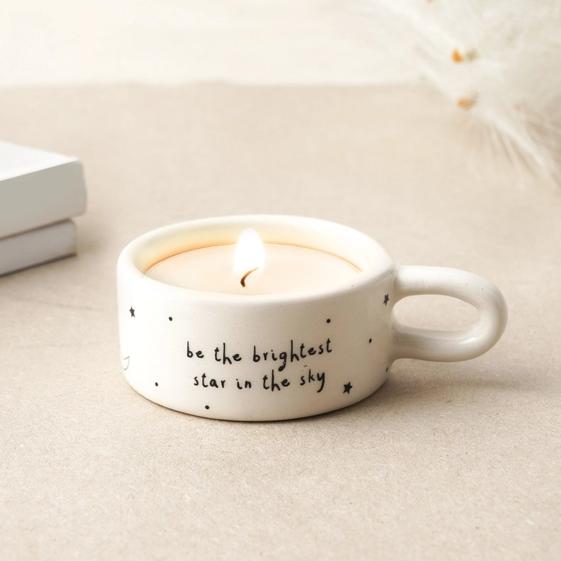 White candle holder with text 'be the brightest star in the sky' on a light surface.