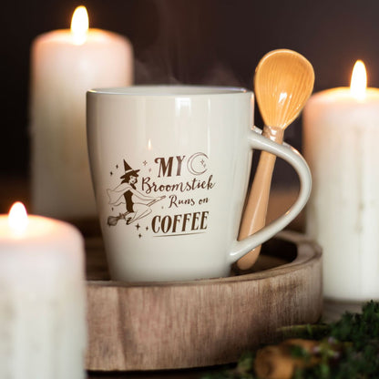 White mug with text 'My Broomstick Runs on Coffee' on a wooden tray with candles in the background