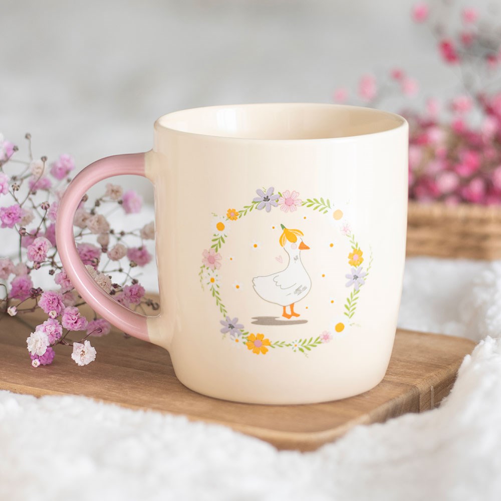 Coffee mug or tea cup with pink handle, floral design and a cute duck illustration in the center.
