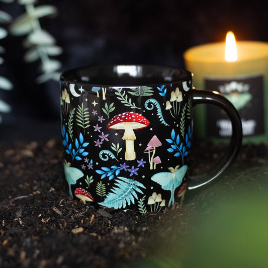 Black mug with colorful forest pattern, mushrooms, moths on a dark background with a candle