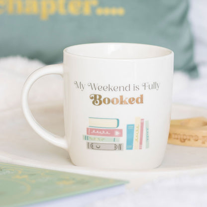 White mug with 'My Weekend is Fully Booked' text and book illustration.