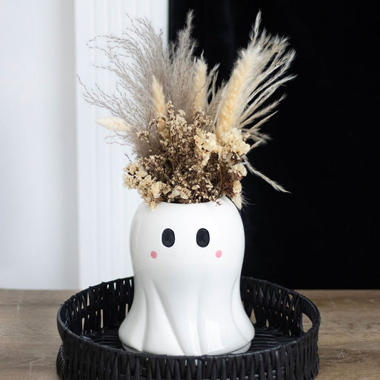Ghost-shaped vase with dried flowers on a black tray against a white curtain background