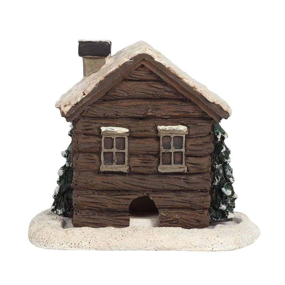 Dark brown log cabin incense cone holder, with snow on the roof and trees on the side.