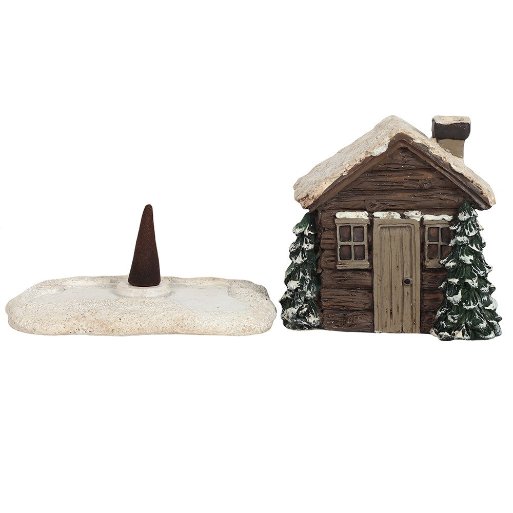 Dark brown log cabin incense cone holder, with snow on the roof and trees on the side.