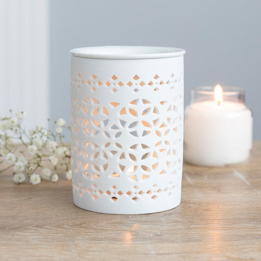 White decorative lantern with cut-out patterns on a wooden surface with a lit candle in the background.