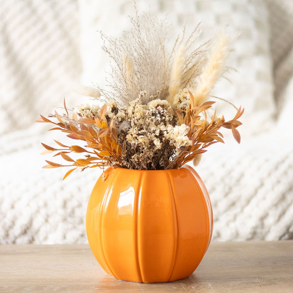 Orange pumpkin-shaped vase with dried flowers on a wooden surface