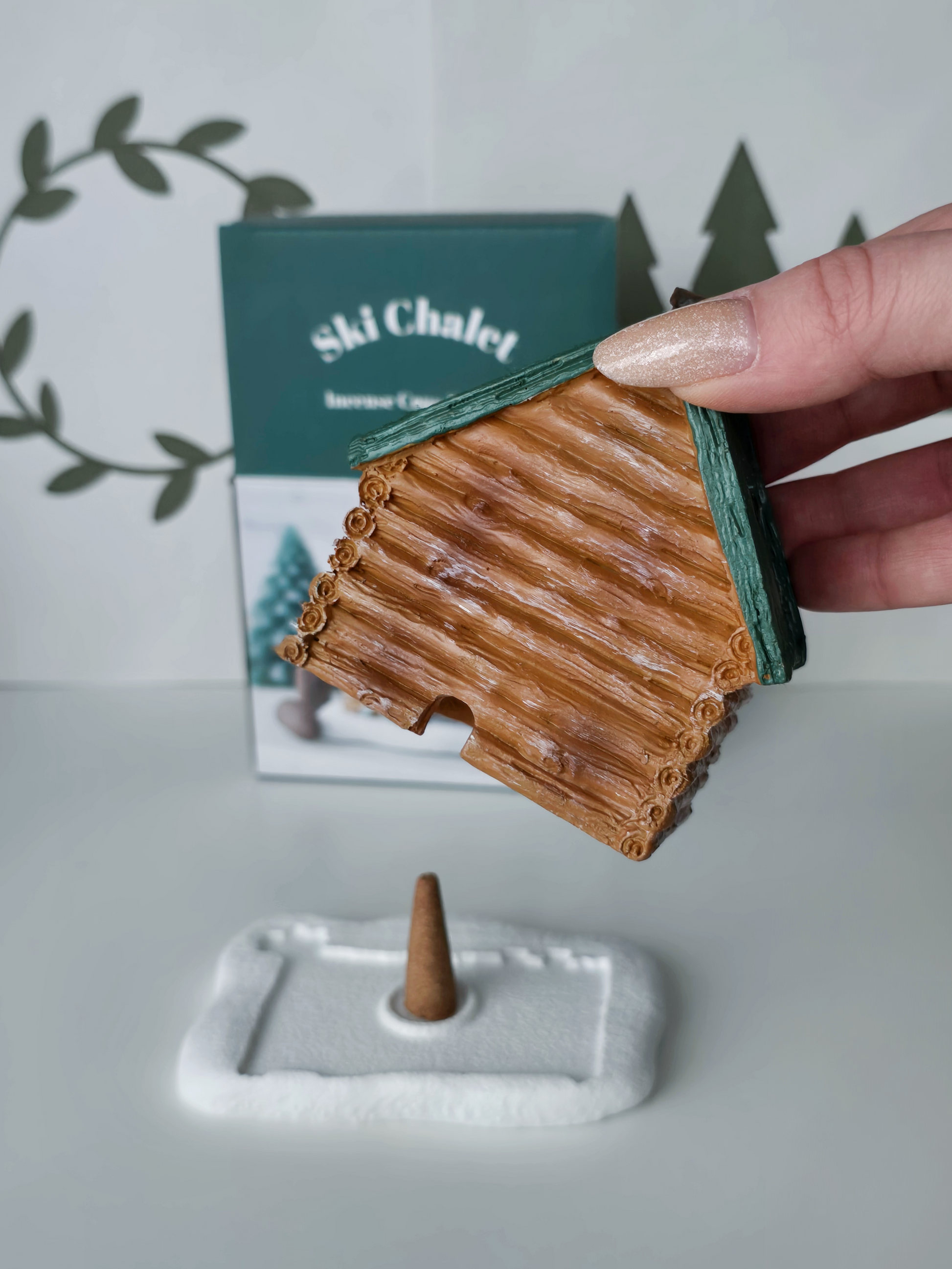 Small wooden cabin model on a stand with a hand holding it, against a light background.