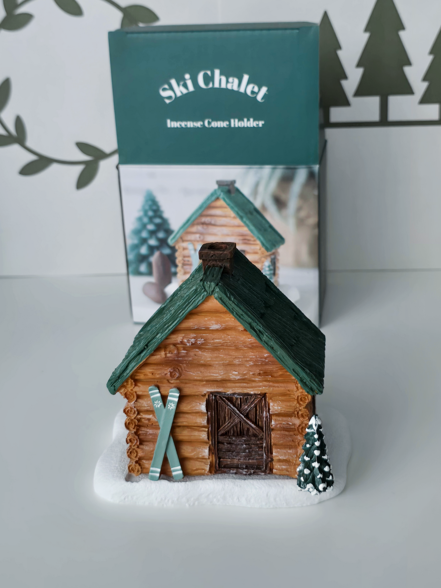 Wooden cabin-shaped incense holder with green roof on a white surface, branded 'Ski Chalet'.