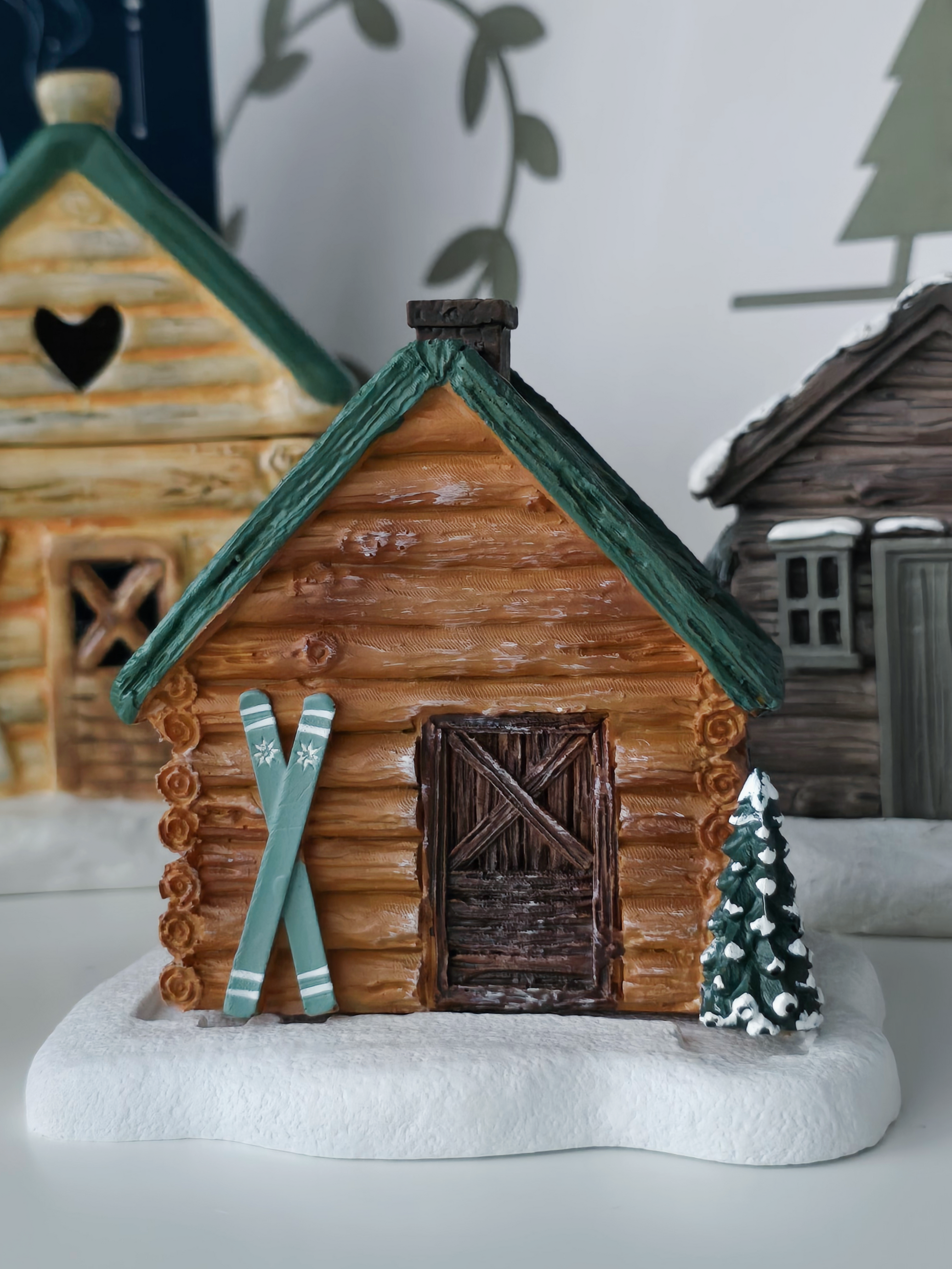Decorative wooden cabin with skis and a small tree on a white surface