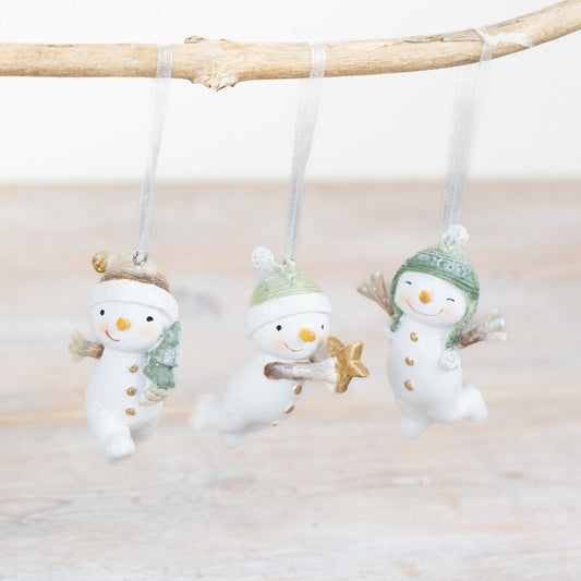 Three snowman ornaments hanging from a branch with a light background