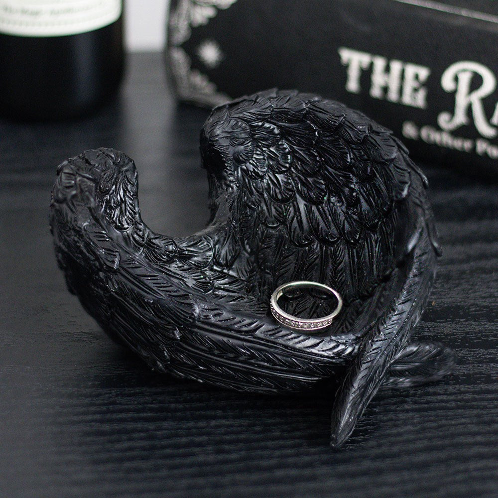 Black accessories holder wing-shaped ring holder with a ring inside, on a dark surface.