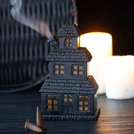 Halloween-themed house decoration with smoke coming out, placed on a dark surface with candles in the background.