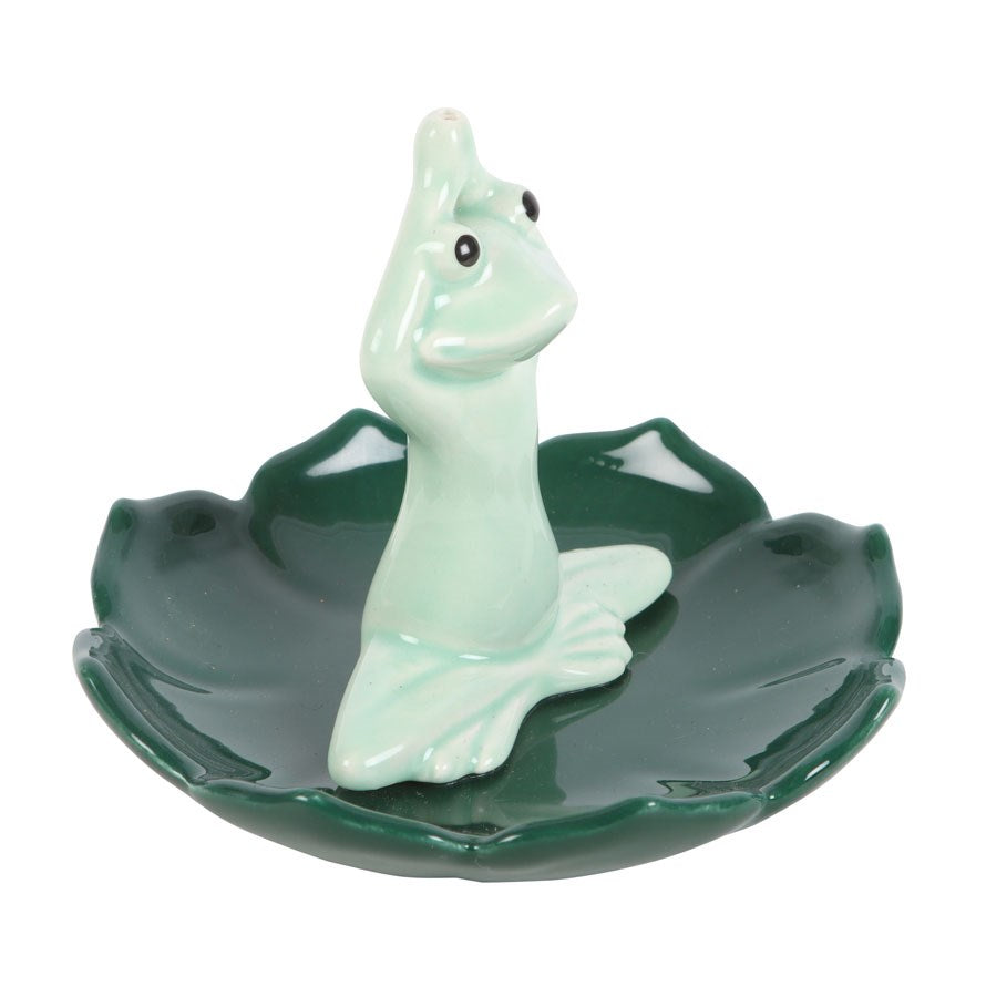 Green ceramic incense stick holder shaped like a pastel green frog that is in a yoga position on a dark green leaf shaped base.