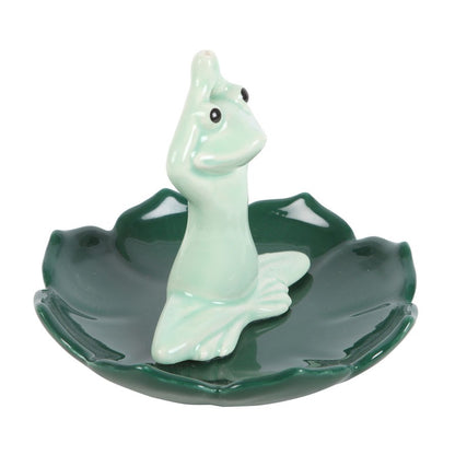 Green ceramic incense stick holder shaped like a pastel green frog that is in a yoga position on a dark green leaf shaped base.